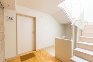 Ein modernes Interieur mit Holzboden, einer weißen Tür mit der Aufschrift 'AL' und einer Treppe mit weißen Geländern.