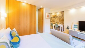 A hotel room with a bed, a TV, a desk, and a stone wall. - Clérigos Tower - Experience in Porto (Porto)