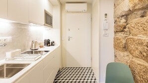 A narrow kitchen with a built-in microwave, a kettle, and a coffee machine. There's a sink with a modern faucet, and a small window above it. The floor has a geometric tile pattern. - Clérigos Tower - Experience in Porto (Porto)
