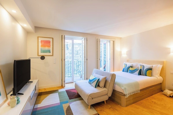 Ein Schlafzimmer mit Bett, Fernseher, Sofa und Balkon.