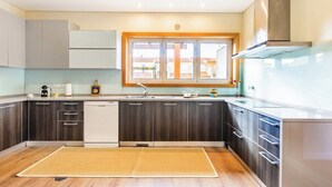 A modern kitchen with dark cabinetry, a dishwasher, and a window with a view of buildings. - Furadouro Holiday Villa | Pool, Tennis & Garden (Ovar)