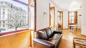 Un salón con un sofá de cuero, una mesa de comedor y un ventanal con vistas a un edificio.