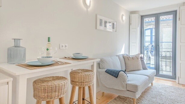 Ein modernes Wohnzimmer mit einem weißen Sofa, einem Esstisch mit Flasche und Gläsern sowie einem Balkon mit blauer Brüstung.
