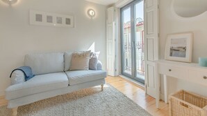 Ein Wohnzimmer mit einer Couch, einem weißen Konsolentisch und einem großen Fenster mit Blick auf einen Balkon.