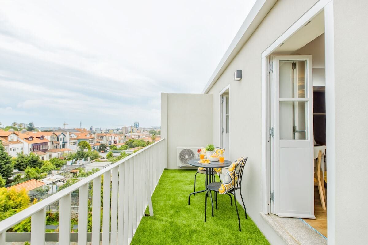 Uma varanda com mesa e cadeiras pequenas, vista para a cidade e guarda-corrimão branco.