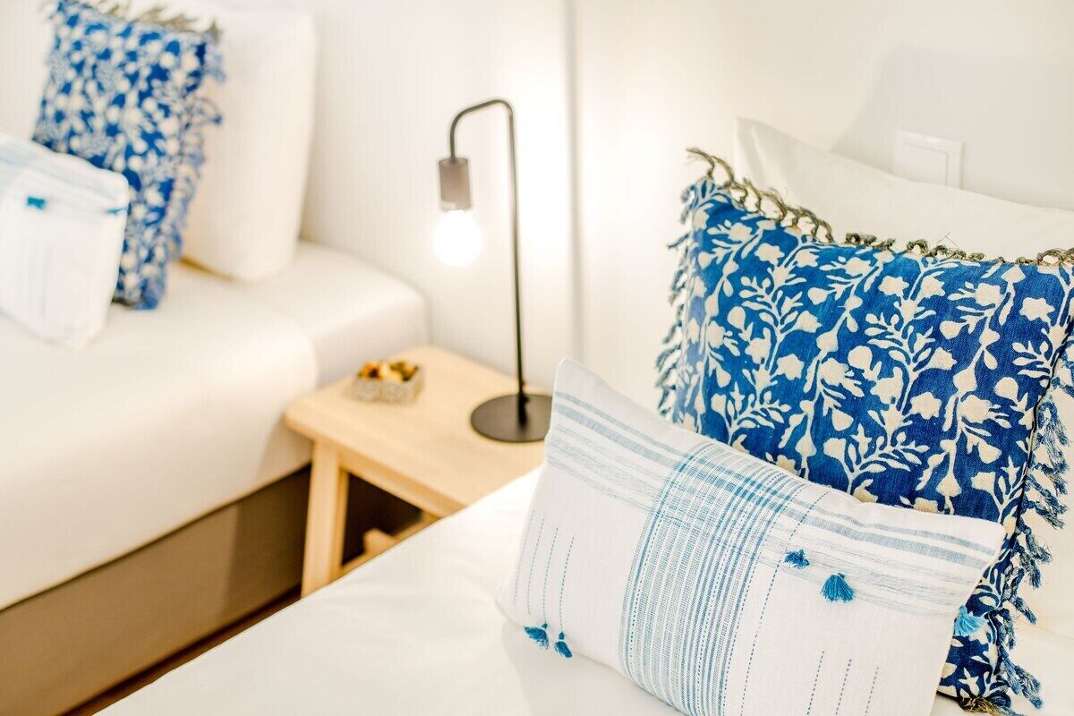 Ett hotellrum med en säng, kuddar, ett sängbord och en lampa.