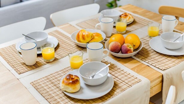 En morgenmadsborddækning med croissanter, frugt og appelsinjuice.