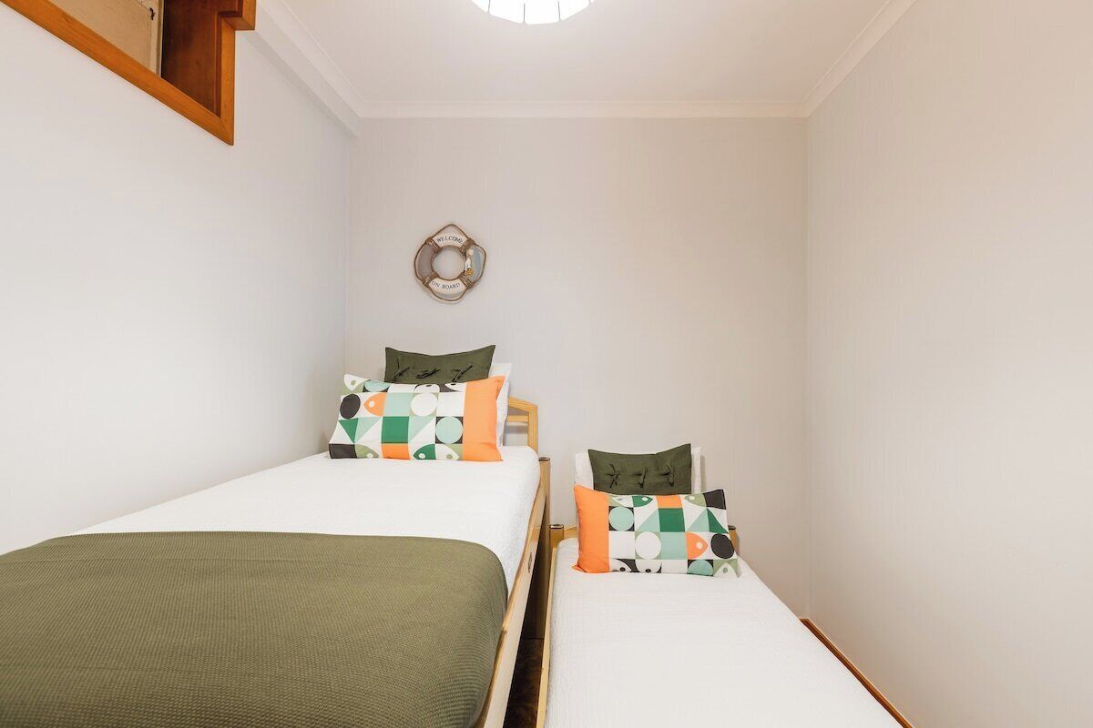 Een kleine, schone kamer met twee bedden, een houten hoofdbord, een wandlamp en een decoratief object aan de muur.