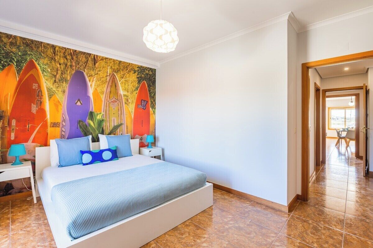 Una camera da letto con un letto, un comodino, una lampada, un affresco raffigurante tavole da surf e un corridoio che conduce a un'altra stanza.