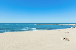 Una spiaggia con un faro in lontananza, una riva sabbiosa e un mare calmo.