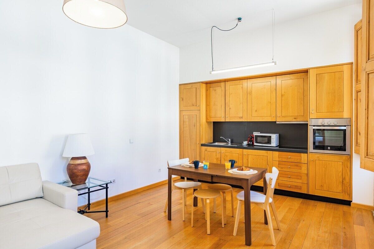 Eine kompakte Küche mit Holzschränken, einem Esstisch mit Stühlen, einer Couch und einer Lampe.