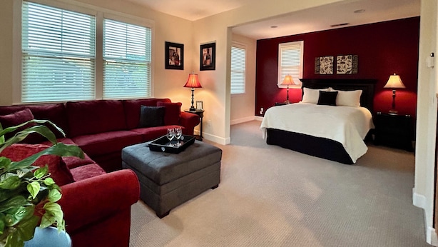 A bedroom with a bed, a red couch, a grey ottoman, and a ceiling fan. - Cozy 1-bedroom studio above detached garage in serene Yountville (Yountville)