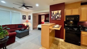 A modern living room with a red couch, a grey ottoman, and a small table with a lamp. There is a kitchen area with a stove, microwave, and cabinets. - Cozy 1-bedroom studio above detached garage in serene Yountville (Yountville)
