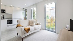 Eine moderne Wohnung mit einem weißen Sofa, einem Fernseher und einem Balkon mit Blick auf Gebäude und Grünflächen.