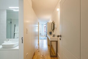 A hallway leading to a bathroom with a white sink and mirror, a door with a handle, and a tiled wall. - Santa Catarina Prime Studios I (Porto)