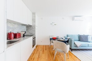 Eine kompakte Küche mit weißen Schränken, einer Marmor-Spritzschutzleiste und einem Essbereich mit einem blauen Sofa und einem Tisch für zwei Personen.