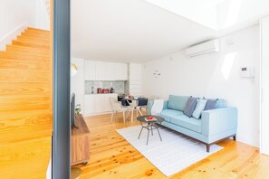 Ein modernes Apartment mit einer Holztreppe, einem hellblauen Sofa, einem Essbereich und einer Küche.