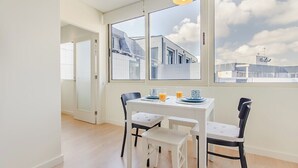 A dining area with a table, chairs, and a view of buildings through large windows. - Trindade Modern Flat (with Air Conditioning) (Porto)