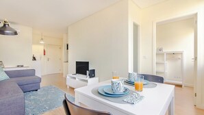 A modern living room with a sofa, a dining table set with blue plates and glasses, and a flat-screen TV. - Trindade Modern Flat (with Air Conditioning) (Porto)