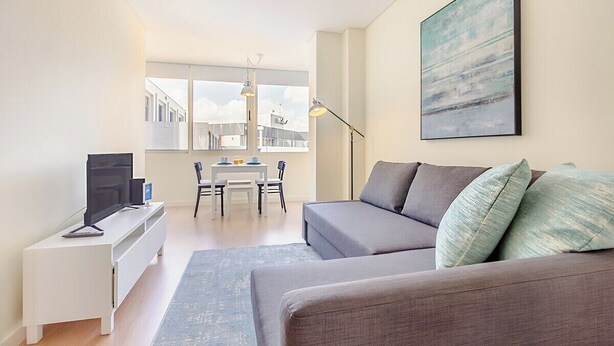 A modern living room with a sofa, a flat-screen TV, a dining table with chairs, and a large window. - Trindade Modern Flat (with Air Conditioning) (Porto)