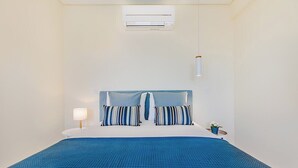 A hotel room with a bed, a bedside table with a lamp, a small potted plant, and an air conditioning unit. - Trindade Modern Flat (with Air Conditioning) (Porto)
