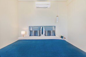 A hotel room with a bed, a bedside table with a lamp, a small potted plant, and an air conditioning unit. - Trindade Modern Flat (with Air Conditioning) (Porto)