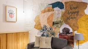 Een gezellige woonkamer met een grijze bank, een houten kast en een muurschildering met een bord waarop staat 'Our happy place'.
