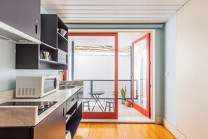 Eine kompakte Küche mit Mikrowelle, Spüle und Schränken, die auf einen Balkon mit Tisch und Stühlen führt.