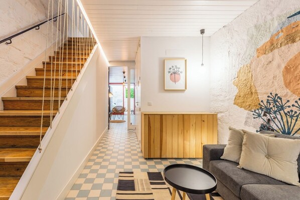 Eine Treppe mit Holzhäuschen und einem weißen Geländer, die zu einem Raum mit Schachbrettfußboden, einer Couch und einem kleinen Tisch führt.
