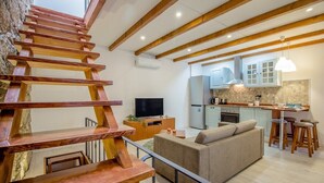 Una cucina moderna con travi in legno, un'area pranzo con sgabelli, un divano e una TV in soggiorno.