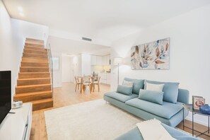 Ein modernes Wohnzimmer mit einer Couch, einem Fernseher, einer Treppe und einem Essbereich.