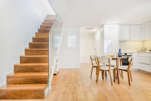 Eine moderne Küche mit weißen Schränken, ein Essbereich mit rundem Tisch und Stühlen sowie eine Holztreppe.