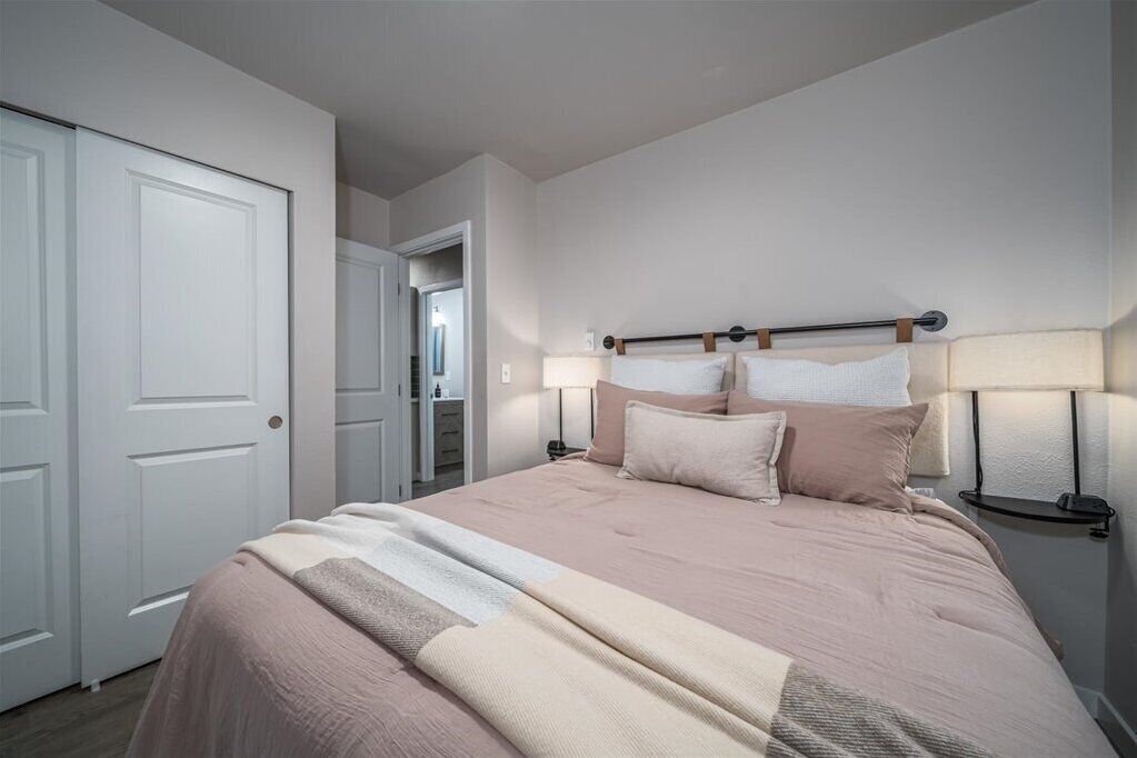 A bedroom with a bed, bedside lamps, and a door.