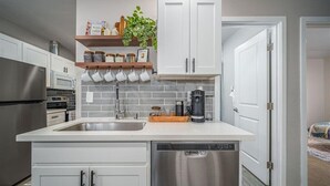Cozinha moderna com armários brancos, eletrodomésticos de aço inoxidável e uma cafeteira sobre a bancada.