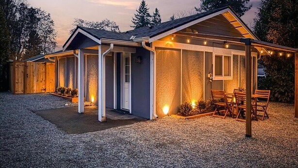 Uma casa moderna com varanda coberta, entrada de cascalho e um pequeno espaço de estar ao ar livre.
