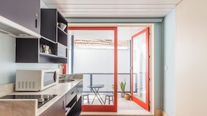 A compact kitchen with a microwave, sink, and cabinets, leading to a balcony with a table and chairs. - Victoria Studios 4 @ Clérigos (Porto)