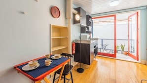 A compact kitchen with a dining table set for two, a small shelf unit, and a red-framed sliding door leading to an outdoor area with a table and chairs. - Victoria Studios 4 @ Clérigos (Porto)