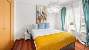 A hotel room with a bed, a nightstand, a painting, and a view of the outdoors. - São Félix Ocean Views | 1BR & Terrace (São Félix da Marinha)