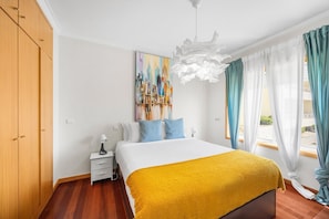 Quarto de hotel com cama, mesa de cabeceira, pintura e vista para o exterior.