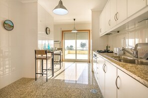 Eine Küche mit weißen Schränken, einer Granit Arbeitsplatte, einem Spülbecken, einem Essbereich mit einem Stuhl und Blick durch eine Glastür.