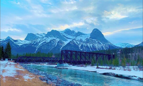 A snow-covered mountain range with a bridge over a river. - CAA Bed & Breakfast Pigeon (Canmore)