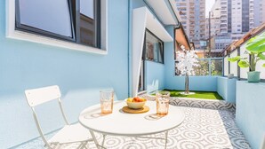 Ein kleiner Balkon mit einem weißen Tisch, zwei Stühlen, einer Obstschale und einem Blumentopf.