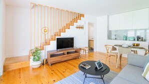 A modern living room with a wooden staircase, a flat-screen TV, a dining area, and a kitchen. - Heroismo Duplex Terrace III (Porto)