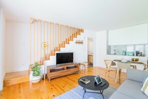 Ein modernes Wohnzimmer mit einer Holztreppe, einem Flachbildfernseher, einem Essbereich und einer Küche.