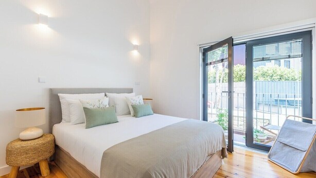 A bedroom with a bed, bedside lamp, and a view of the outdoors through a sliding door. - Heroismo Duplex Terrace III (Porto)