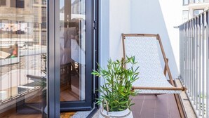 A balcony with a sliding glass door, a wooden chair, a woven basket with plants, and a patterned mat. - Heroismo Duplex Terrace III (Porto)