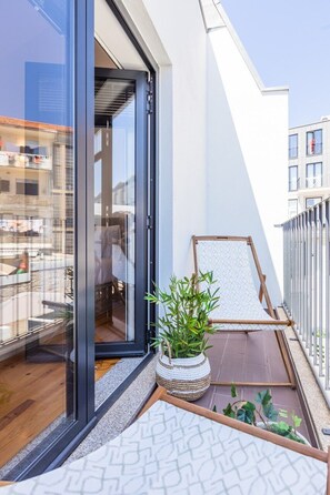 Ein Balkon mit einer Schiebetür aus Glas, einem Holzstuhl, einem gewebten Korb mit Pflanzen und einer gemusterten Matte.