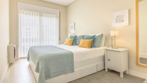 Ein Schlafzimmer mit Bett, Nachttischen, einem Fenster mit Jalousien und Wandbildern.
