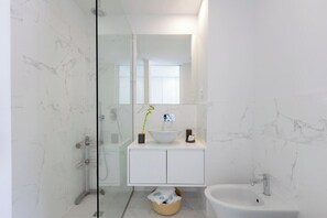 Ein modernes Badezimmer mit Duschkabine aus Glas, einem weißen Waschbecken mit Marmorplatte und einem Bidet.