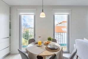 Ein Essbereich mit einem für das Frühstück gedecktem Tisch, großen Fenstern und Blick auf Gebäude.